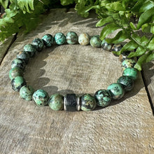 Vihreä rannekoru puisella alustalla vihreitä lehtiä taustalla.