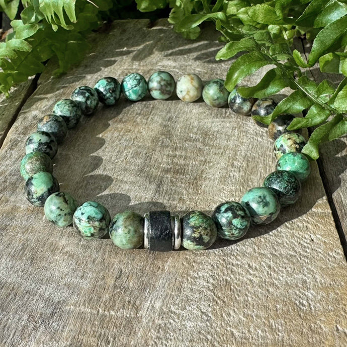 Vihreä rannekoru puisella alustalla vihreitä lehtiä taustalla.