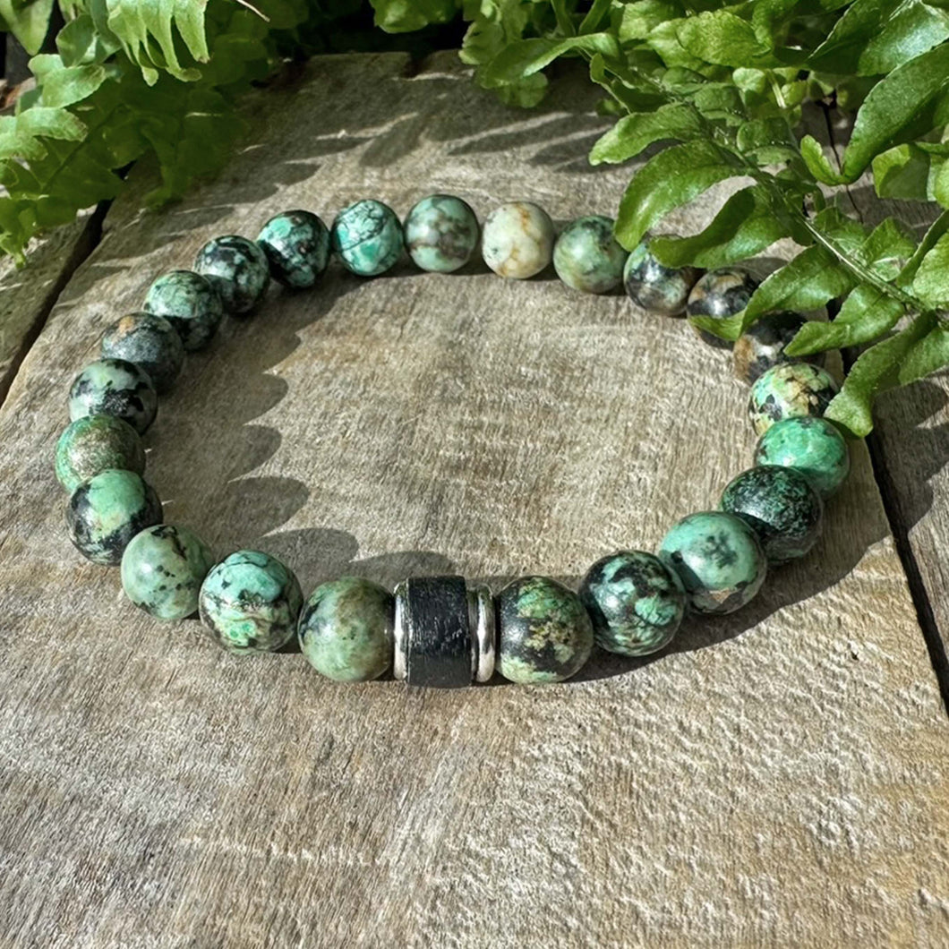 Vihreä rannekoru puisella alustalla vihreitä lehtiä taustalla.